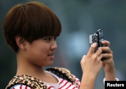 Seorang remaja perempuan memegang dua ponsel saat berfoto di pusat kota Shanghai, 22 Oktober 2012.