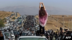 Seorang perempuan tak berjilbab berdiri di atas kendaraan saat ribuan orang berjalan menuju pemakaman Mahsa Amini. Iran memasang CCTV di tempat umum dan jalan raya untuk mengendalikan peningkatan jumlah perempuan yang menentang aturan berpakaian negara itu. (Foto: AFP)