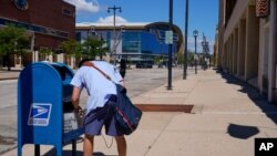 In this Aug. 18, 2020, file photo, a postal worker empties a box near the Fiserv Forum in Milwaukee. U.S. Postal Service records show delivery delays have persisted across the country as millions of Americans began voting by mail.