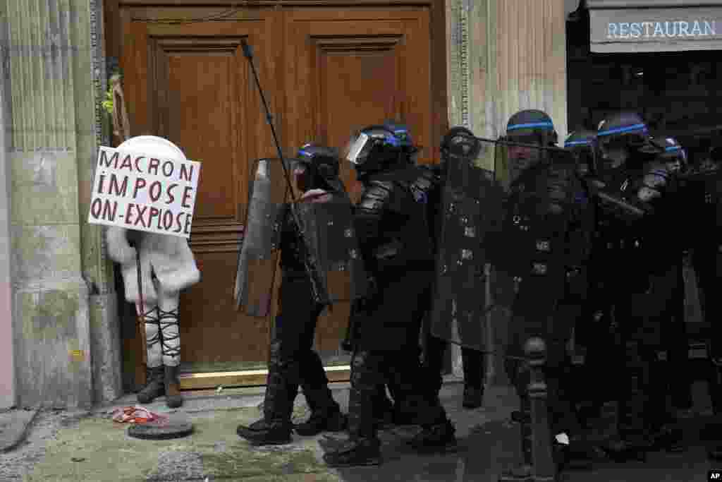 Seorang pengunjuk rasa bersembunyi di balik poster bertuliskan "Macron memaksa, kami meledak" selama demonstrasi menentang rencana tidak populer Presiden Prancis Emmanuel Macron untuk menaikkan usia pensiun, di Paris, Prancis.