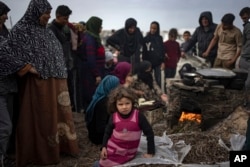 Seorang gadis kecil duduk ketika warga Palestina yang mengungsi akibat pengeboman Israel menunggu giliran untuk memanggang roti di tenda kamp darurat di daerah Muwasi di Rafah, Jalur Gaza, 23 Desember 2023. (Foto: AP)