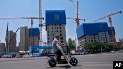 Seorang pria berkendara melewati gedung-gedung yang sedang dibangun di Beijing, 5 Juni 2023. Dana Moneter Internasional mengatakan perlambatan ekonomi China kemungkinan akan terus berlanjut selama empat tahun ke depan. (Foto: Andy Wong/AP Photo)