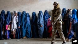 Seorang anggota Taliban berjaga saat kaum perempuan menunggu untuk menerima jatah makanan yang didistribusikan oleh kelompok bantuan kemanusiaan, di Kabul, Afghanistan, 23 Mei 2023. (Foto: AP)