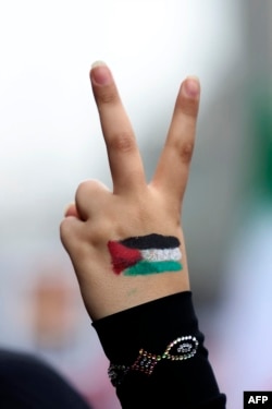 Seorang perempuan mengacungkan tangan bergambar bendera Palestina dan jarinya membentuk tanda kemenangan dalam unjuk rasa di luar bekas gedung Kedutaan Besar AS di Teheran , Iran, Sabtu, 4 November 2023. (Foto: Atta Kenare/AFP)