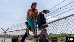 Seorang perempuan migran membantu putranya memanjat pagar kawat berduri setelah melintasi sungai Rio Grande dari Meksiko untuk memasuki kota Eagle Pass, Texas di Amerika Serikat (foto: ilustrasi). 