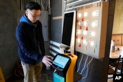 Li Zhai dari restoran Noodle Topia menunjukkan fitur pada robot BellaBot miliknya, Senin, 20 Maret 2023 di Madison Heights, Michigan. (AP/Carlos Osorio)