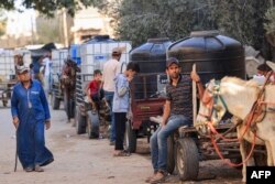 Warga Palestina berkumpul di samping gerobak yang ditarik keledai yang berisi tangki air untuk dijual, ketika air minum dan bahan bakar semakin langka, di Khan Yunis di selatan Jalur Gaza, 30 Oktober 2023. (Foto: AFP)