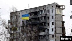A Ukrainian national flag flies in front of a destroyed residential building amid Russia's invasion of Ukraine, in Borodianka, Kyiv region, Feb. 18, 2023. 