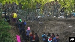 Texas state police finish placing barbed-wire as migrants walk up the bank of the Rio Grande river, seen from Matamoros, Mexico, May 10, 2023. 