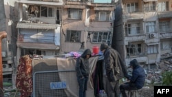 Displaced quake-hit residents huddle next to their makeshift tent near collapsed buildings in Hatay, Turkey, on Feb. 15, 2023, nine days after a 7.8 magnitude earthquake struck parts of Turkey and Syria.
