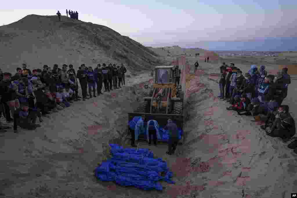 Petugas memindahkan jenazah warga Palestina yang tewas dalam pertempuran dengan Israel dari buldoser yang diserahkan oleh militer Israel, dalam pemakaman massal di Rafah, Jalur Gaza.