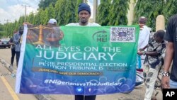 A man holds a banner in Abuja, Nigeria, Sept. 6, 2023, as Nigeria's presidential tribunal met to deliver its judgment on the disputed election of Bola Tinubu as president. The tribunal upheld the election.