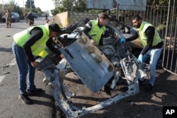 Sejumla pekerja membersihkan puing-puing mobil yang hancur di Kota Bazouriyeh, Lebanon, Sabtu, 20 Januari 2024. Serangan drone Israel terhadap mobil di dekat kota pelabuhan Tire di Lebanon menewaskan dua orang. (Foto: Mohammad Zaatari/AP Photo)