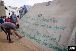A man writes a message of thanks to students in the U.S. protesting in solidarity with the people of Gaza, on a tent at a camp for displaced Palestinians in Rafah, in the southern Gaza Strip, April 27, 2024.