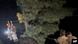 In this image made from video, military and local rescue workers bring people from a dangling cable car to safety using ropes and harnesses in Battagram district in Khyber Pakhtunkhwa province, Pakistan, on Aug. 22, 2023. (Pakistan Rescue Military via AP)