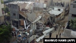 Orang-orang berkumpul di depan bangunan yang terkena serangan udara oleh Israel di Kota Gaza, Sabtu, 13 Mei 2023. Israel dan Gaza saling menembakan artileri berat pada 12 Mei, tetapi Mesir berhasil memediasi untuk menghentikan konflik. (Foto: Mahmud Hams/AFP)