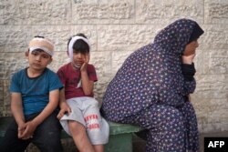Dua anak laki-laki Palestina bersama kerabat di RS Martir Al-Aqsa di Deir al-Balah, di Jalur Gaza, menunggu giliran mengidentifikasi jenazah kerabat lainnya yang tewas dalam pengeboman oleh Israel, Sabtu, 11 Mei 2024. (Foto: AFP)