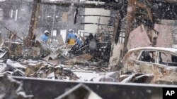 Salju turun saat petugas polisi melanjutkan operasi pencarian di sekitar pasar yang terbakar di Wajima usai gempa, prefektur Ishikawa, Jepang, 7 Januari 2024. (Foto: Kyodo via AP)
