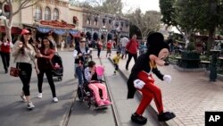 FILE - Visitors follow the Mickey Mouse character for photos at Disneyland in Anaheim, California, Jan. 22, 2015.