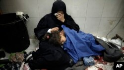 یک زن فلسطینی در شفاخانهٔ ناصر واقع در منطقهٔ خان یونس غزه در کنار دخترنسشته است که حملات نوار غزه زخمی شده است.