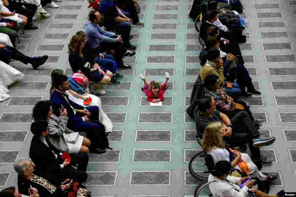 Seorang anak bermain di lantai saat berlangsungnya audiensi umum mingguan di aula Paulus VI di Vatikan, 1 Mei 2024. (REUTERS/Remo Casilli)