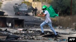 A Palestinian youth holds a Hamas flag during confrontations with Israeli troops at the northern entrance of Ramallah, West Bank, near the Israeli settlement of Beit El, Oct. 27, 2023, as battles continue between Israel and Hamas.