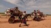 A Sudanese woman, who fled the conflict in Murnei in Sudan's Darfur region, walks beside carts carrying her family belongings upon crossing the border between Sudan and Chad in Adre, Chad, Aug. 2, 2023. 
