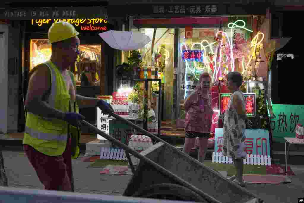 A worker pushes a cart past stores in Beijing, Aug. 15, 2023.