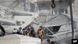 Sejumlah petugas layanan darurat bekerja di sebuah gedung yang terkena serangan udara di Damaskus, Suriah, Sabtu, 20 Januari 2024. Media pemerintah Suriah dan Iran mengatakan serangan Israel di ibu kota Suriah menewaskan lima penasihat Iran. (Foto: Omar Sanadiki/AP Photo)