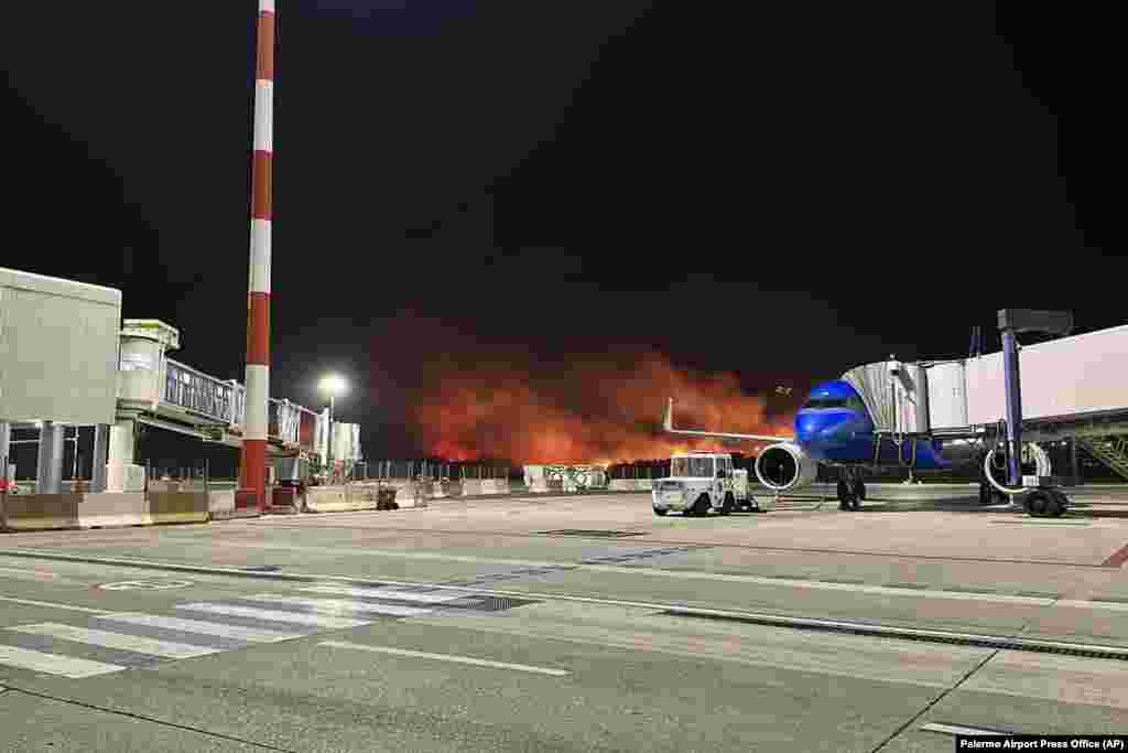 Plumes of fire and smoke cover the hills surrounding Palermo's airport, Sicily, Italy, late Monday night, July 24, 2023, causing its shutdown and leaving planes trapped on the tarmac. The airport reopened on July 25 only for departing planes. 