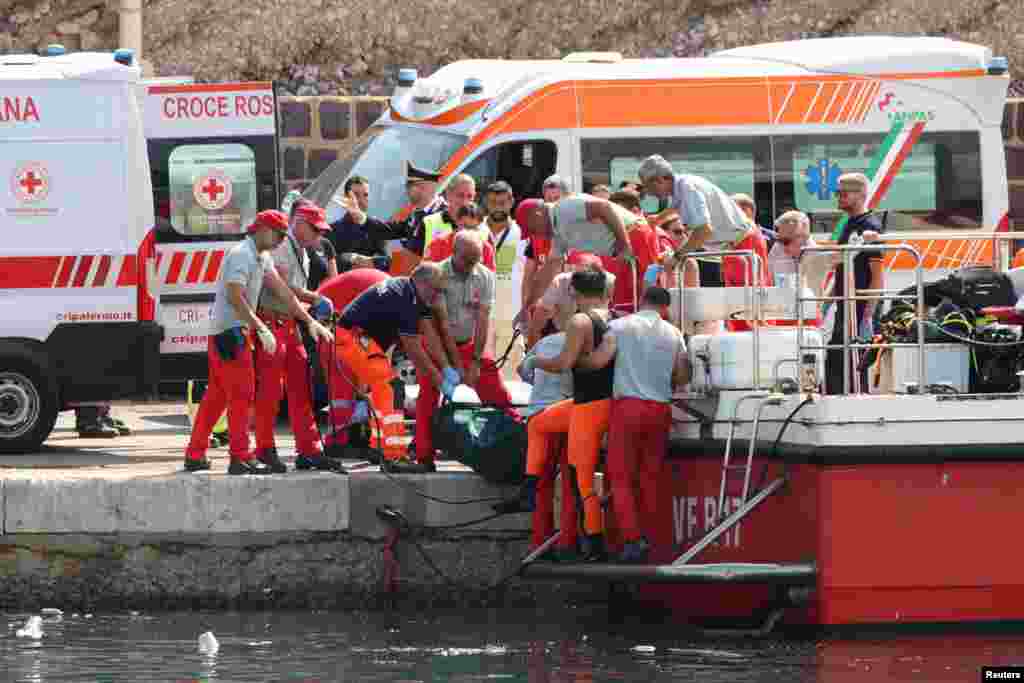 Emergency service members carry a body bag after a sailboat sank in the early hours of Monday, off the coast of Porticello, near the Sicilian city of Palermo, Italy. One man died and six people were missing, including British tech entrepreneur Mike Lynch, after a luxury yacht was struck by an unexpectedly violent storm and sank off Sicily.