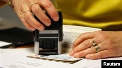 FILE - An employee validates an extension visa on a foreign student's passport at a foreign visas office in Paris, Nov. 18, 2011.