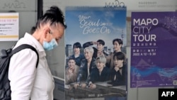Seorang perempuan berjalan melewati poster yang memperlihatkan anggota grup K-pop BTS di pusat informasi turis di Seoul pada 15 Juni 2022. China menangguhkan pemberian visa bagi warga Korea Selatan yang akan datang ke negara itu.(Foto: AFP/Jung Yeon-je)