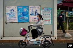 Seorang perempuan melewati fasilitas pengujian virus corona yang memajang poster kampanye vaksinasi COVID-19 di Beijing, Rabu, 26 Oktober 2022. Kota Shanghai di China mulai memberikan vaksin COVID-19 yang dapat dihirup pada hari Rabu di tempat yang tampaknya menjadi yang pertama di dunia . (AP/Andy Wong)