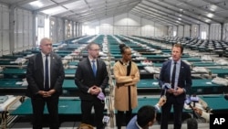 New York City Emergency Management Commissioner Zach Iscol, far right, and other officials talk with reporters in the sleeping area of the city's latest temporary shelter on Randall's Island, Oct. 18, 2022.