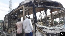 Orang-orang memeriksa bus transportasi pemerintah yang dibakar di stasiun Berger dekat Ikeja, Lagos, Nigeria, 22 Oktober 2020. (Foto: AP)