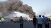 Orang-orang memperhatikan asap yang membubung dari serangan misil ke sebuah gudang milik perusahaan perdagangan di Odessa, 16 Juli 2022 di tengah invasi Rusia ke Ukraina. (Foto: Oleksandr Gimanov/ AFP)