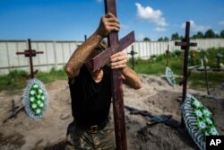 Seorang pekerja pemakaman memasang salib di kuburan seorang warga sipil tak dikenal yang dibunuh oleh pasukan Rusia selama pendudukan Rusia di Bucha dekat Kyiv, Ukraina. (Foto: AP)