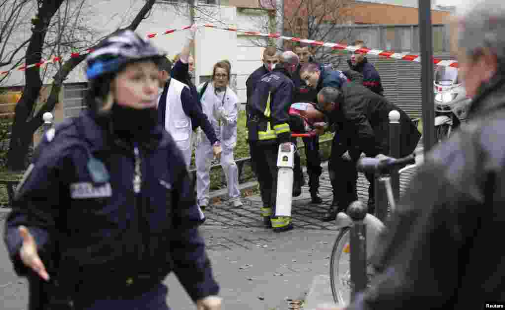 Petugas pemadam kebakaran membawa korban dari lokasi penembakan di kantor koran satiris Charlie Hebdo, Paris (7/1).