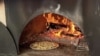 Pizza ທີ່ເປັນສູດຂອງທາງຮ້ານ, ກໍາລັງອົບຢູ່ໃນເຕົາຟືນ ເພື່ອເອົາໄປສົ່ງໃຫ້ລູກຄ້າຕາມການສັ່ງຈອງທາງອອນລາຍ.