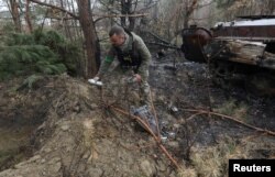 Seorang personel mengambil bagian dari bom klaster yang tidak meledak setelah invasi Rusia dekat desa Motyzhyn, wilayah Kyiv, Ukraina, 10 April 2022. (Mykola Tymchenko/Reuters)