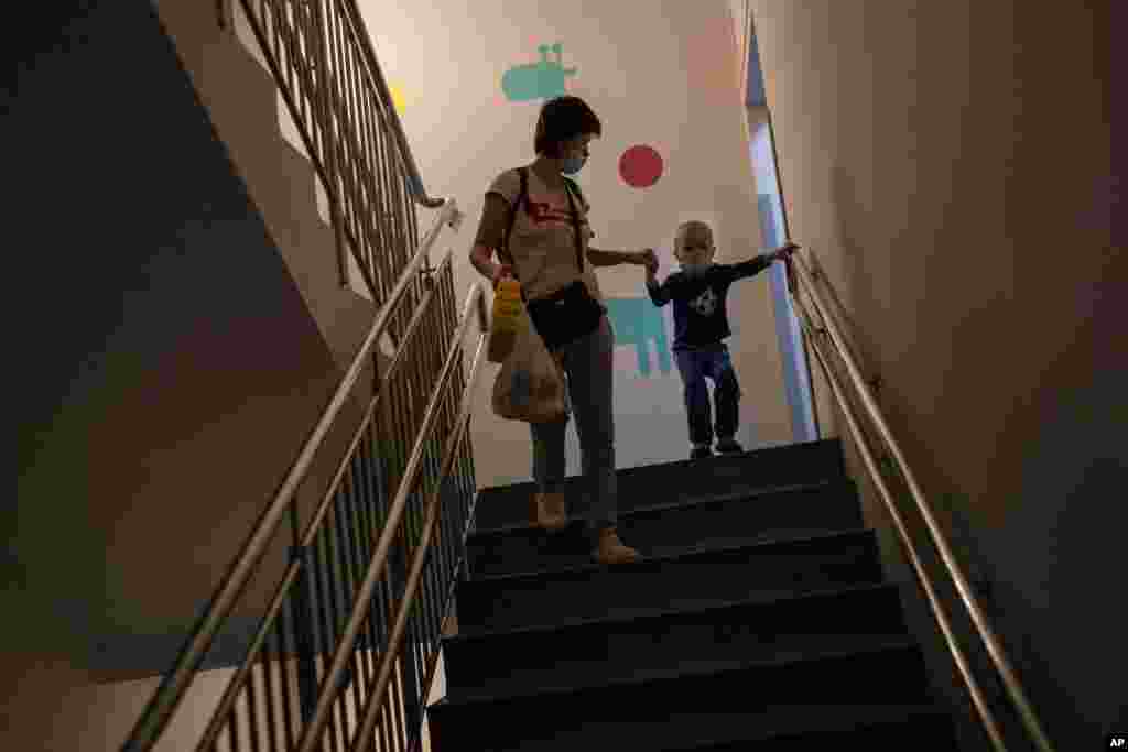A woman with her son admitted to oncology walks down the stairs to take shelter in a basement used as a bomb shelter, while the sirens sound announcing new attacks, at the Okhmadet children's hospital in central Kyiv, Ukraine, Feb. 28, 2022.
