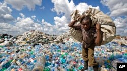FILE - A man walks on a mountain of plastic bottles as he carries a sack of them to be sold for recycling after weighing them at the dump in the Dandora slum of Nairobi, Kenya, on Dec. 5, 2018. 