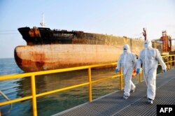 Petugas inspeksi imigrasi China dengan pakaian pelindung berjalan melewati kapal tanker minyak di pelabuhan di Qingdao, di provinsi Shandong timur China. (Foto: AFP)