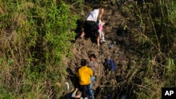A Venezuelan migrant grips a child as he climbs a river bank onto U.S territory, after crossing from Matamoros, Mexico, Dec. 22, 2022.