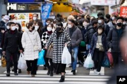 Publik menenteng tas belanjaan mereka, berjalan melintasi persimpangan lalu lintas menuju stasiun kereta di distrik Ueno sebelum liburan Tahun Baru di Tokyo, Jumat, 30 Desember 2022. (AP Photo/Hiro Komae)