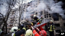 In this photo released by Ukrainian State Emergency Service, firefighters evacuate a man from an apartment building hit by shelling in Kyiv, Ukraine, March 14, 2022. 