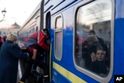 A man helps a disabled elderly Ukrainian to board a train as a child waves, at the train station in Odesa, southern Ukraine, March 23, 2022.