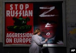 Seorang perempuan berjalan melewati dinding dengan poster yang menggambarkan Presiden Rusia Vladimir Putin, kanan, di Warsawa, Polandia, 24 Maret 2022. (Foto: AP)