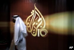 FILE - A Qatari employee of Al Jazeera Arabic language TV news channel walks past the logo of Al Jazeera in Doha, Qatar,